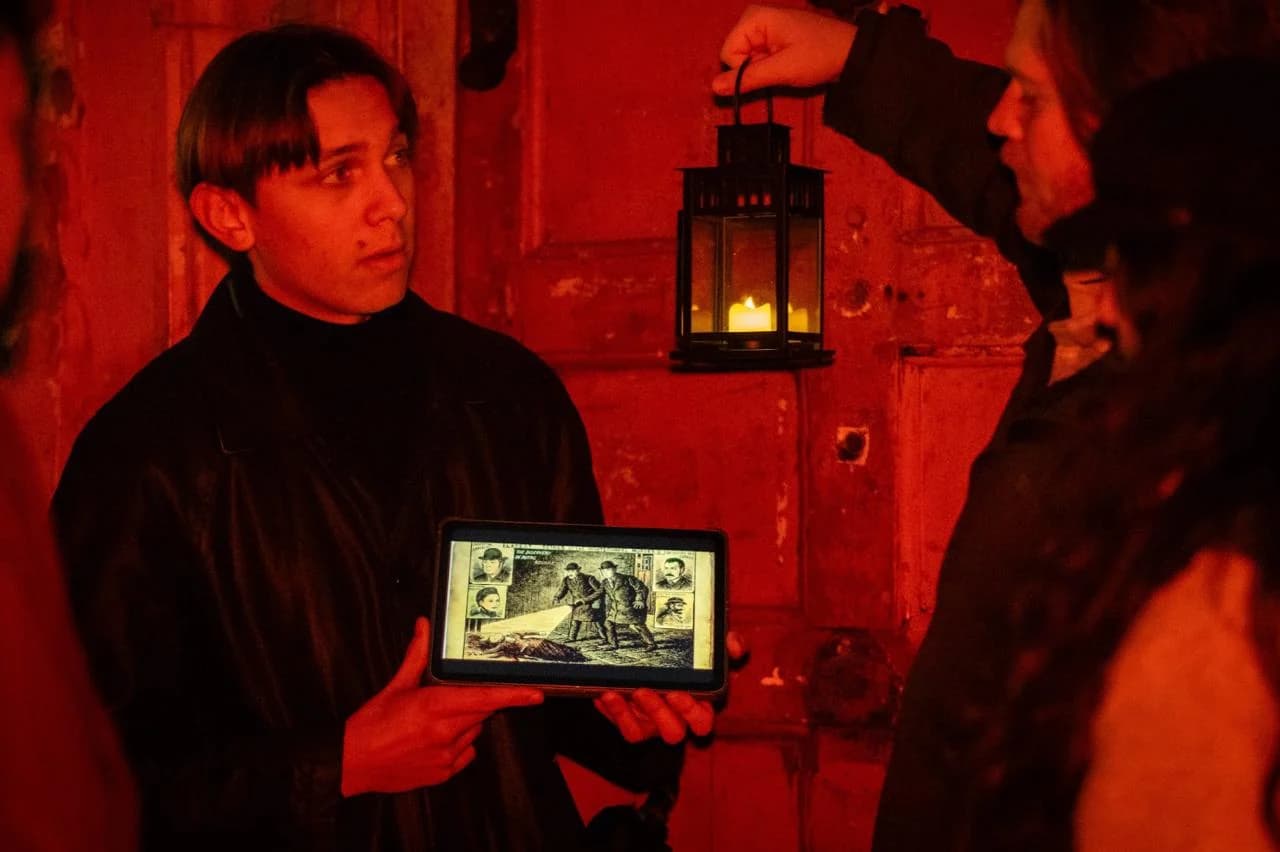 A Jack the Ripper tour guide using a tablet during a lantern-lit Whitechapel tour