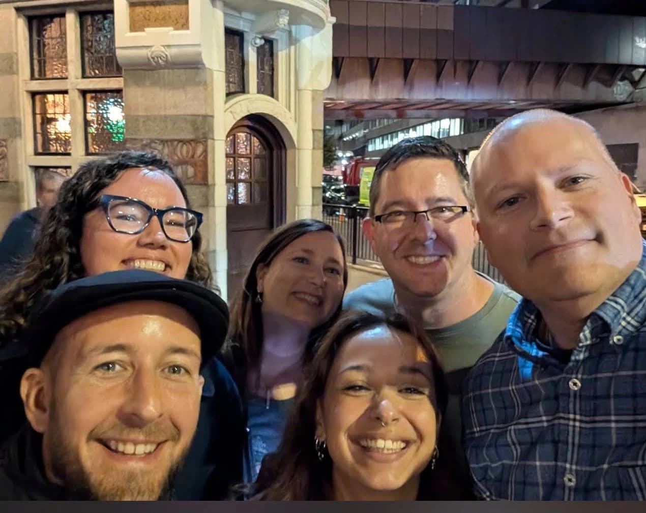 Six smiling guests taking a group selfie at night during a Jack the Ripper tour in London.